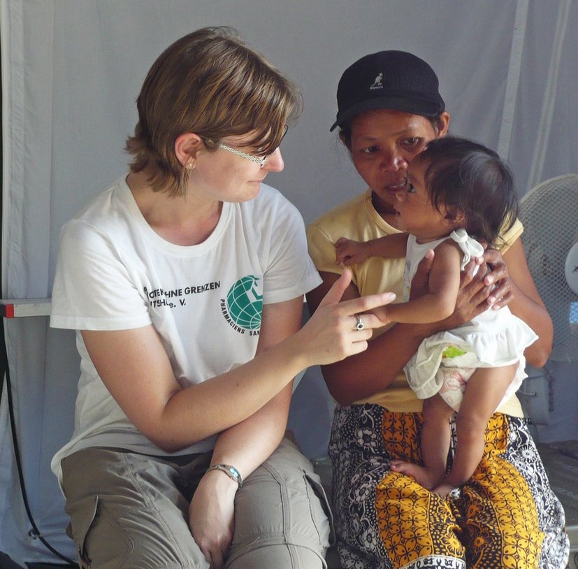 Eine Frau in weißem T-Shirt spricht mit einer anderen Frau, die ein Baby auf dem Schoß hält.
