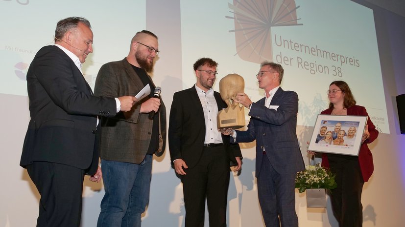 Gruppe von Menschen bei der Verleihung des Unternehmerpreises der Region 38, lächelnd mit einer Trophäe und Urkunde.