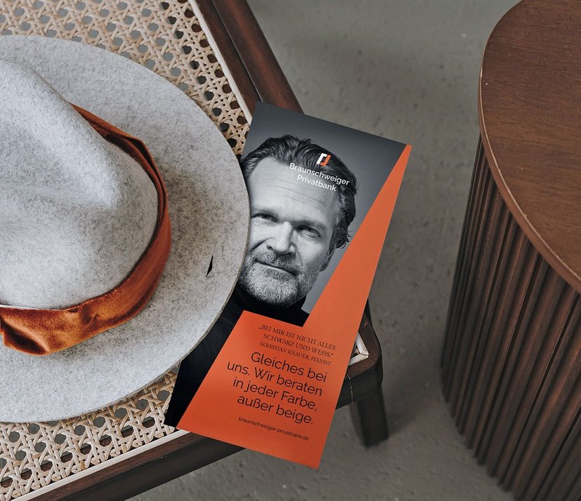 Flyer der Braunschweiger Privatbank auf Tisch mit Hut, Slogan: "Gleiches bei uns. Wir beraten in jeder Farbe, außer beige."