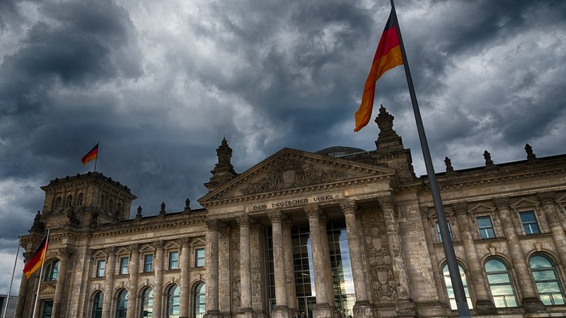 Dramatischer Himmel über dem Reichstagsgebäude in Berlin mit wehenden deutschen Flaggen.
