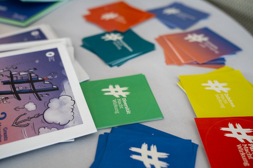 Bunte Karten und Broschüren auf einem Tisch, Hashtag-Design, Text: Diversität Macht Wirkung.