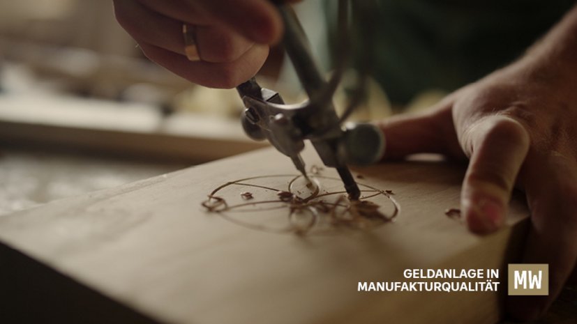 Detailaufnahme von Händen, die mit einem Zirkel ein präzises Muster in ein Holzbrett gravieren, Text: Geldanlage in Manufakturqualität.