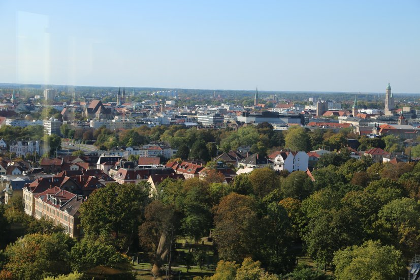 Stadtansicht mit grünem Park im Vordergrund und historischen Gebäuden im Hintergrund bei klarem Himmel.