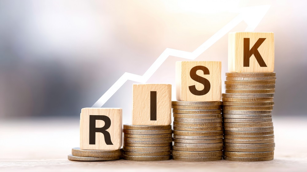 Holzbuchstaben auf Münzstapeln bilden das Wort "RISK", hinterlegt von einem ansteigenden Pfeil.
