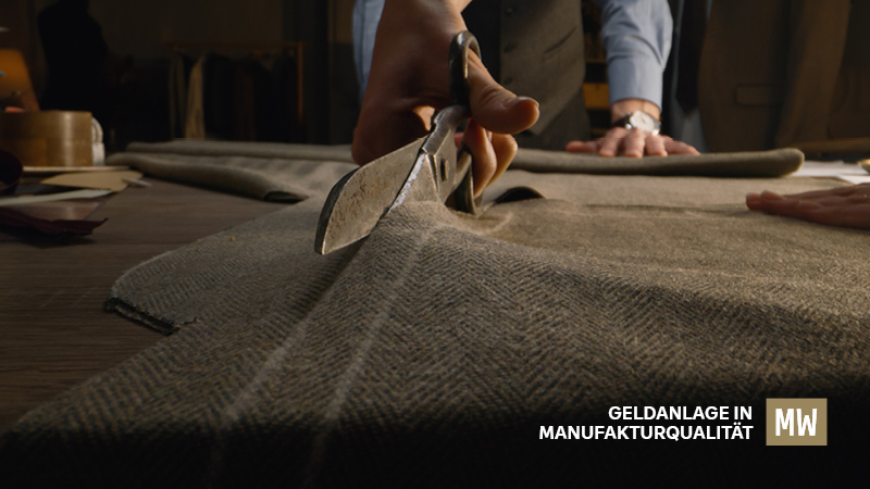 Eine Person schneidet mit einer Schere einen Anzugstoff, daneben der Text: Geldanlage in Manufakturqualität.